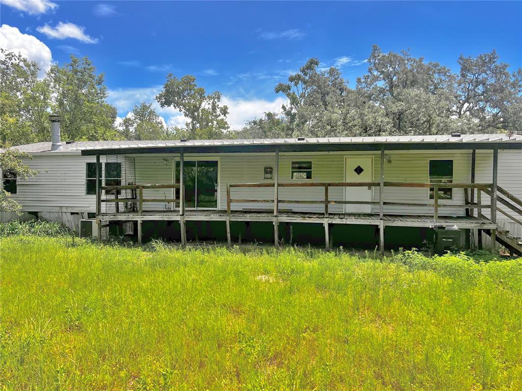 A single-story manufactured home with a long wooden deck sits in a grassy field — 6487 SPINNER DRIVE, LAKE WALES, FL