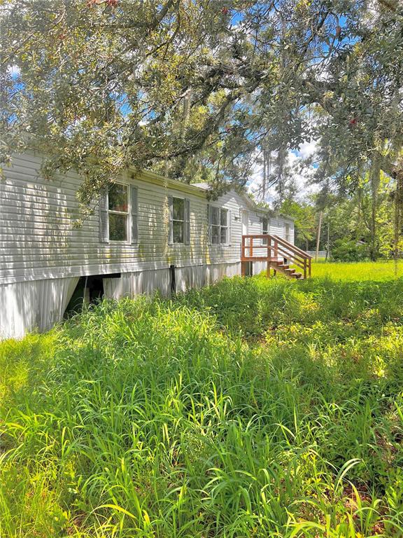 A single-story mobile home with light siding stands in a yard with tall, overgrown grass — 6487 SPINNER DRIVE, LAKE WALES, FL