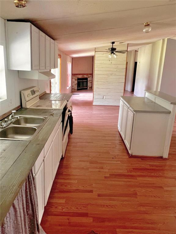 A kitchen with white cabinets, a double sink, and wood flooring leads to a fireplace — 6487 SPINNER DRIVE, LAKE WALES, FL