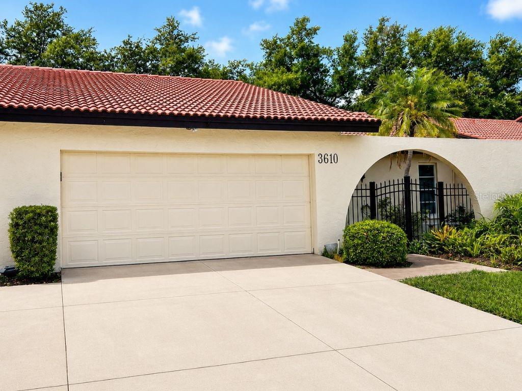 A beige house exterior features a two-car garage, a tiled roof, and an arched entryway — 3610 NARANJA WAY UNIT 8510, SARASOTA, FL