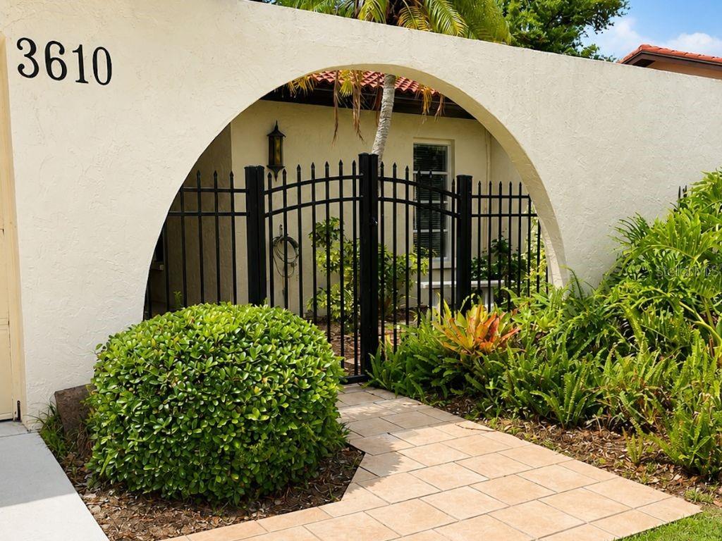 A gated entryway features a rounded archway, a tiled walkway, and lush landscaping — 3610 NARANJA WAY UNIT 8510, SARASOTA, FL
