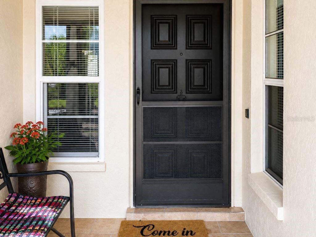 A front porch features a black storm door, a potted plant, and a welcome mat — 3610 NARANJA WAY UNIT 8510, SARASOTA, FL