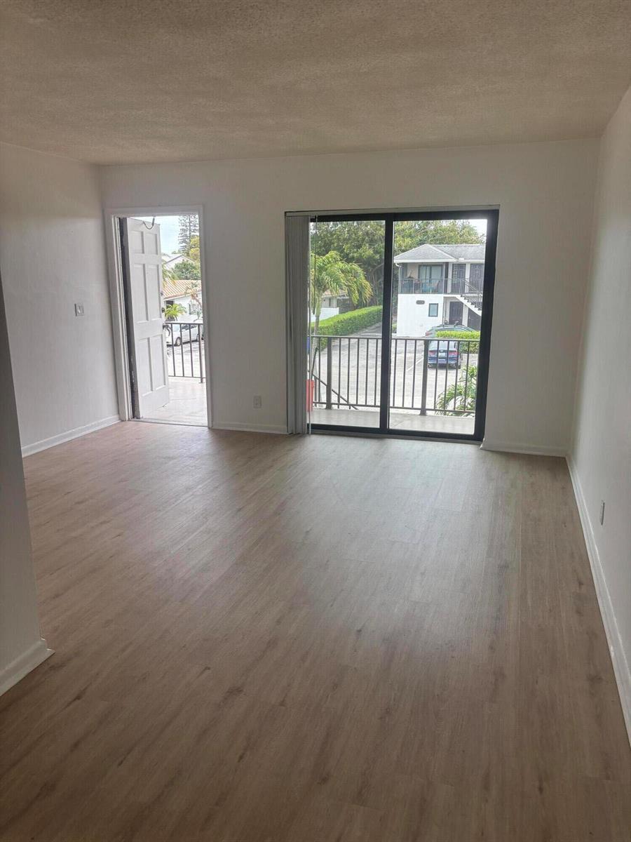 An empty room with light wood-look flooring, white walls, a balcony door, and sliding glass doors — 521 NE 45th Street, Boca Raton FL 33431, BOCA RATON, FL