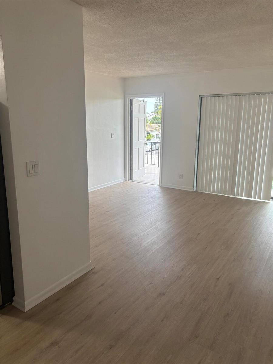 An interior view of a living area with light wood-look flooring and a balcony door — 521 NE 45th Street, Boca Raton FL 33431, BOCA RATON, FL