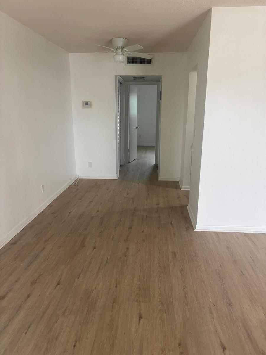 An empty room with light wood-look flooring leads to a hallway and an open doorway — 521 NE 45th Street, Boca Raton FL 33431, BOCA RATON, FL