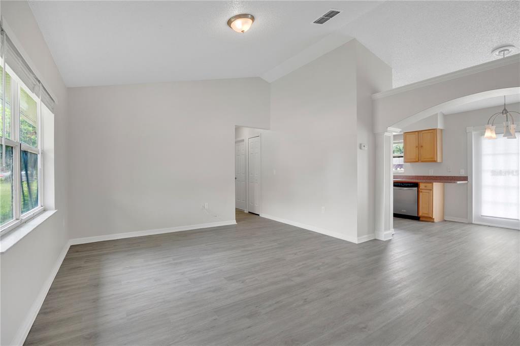 A living room with light gray walls, wood-look flooring, and an adjacent kitchen area — 3023 INDIA BOULEVARD, DELTONA, FL