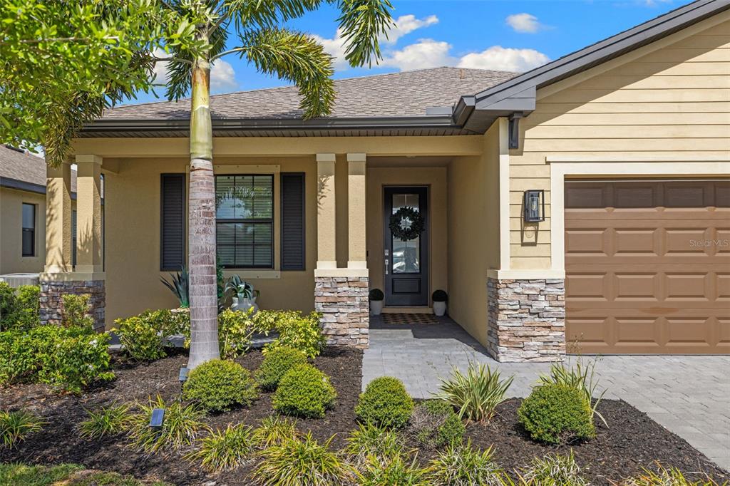 The exterior of a single-story house features a stone-accented porch, a palm tree, and a garage — 1842 W ISLES ROAD, PORT CHARLOTTE, FL