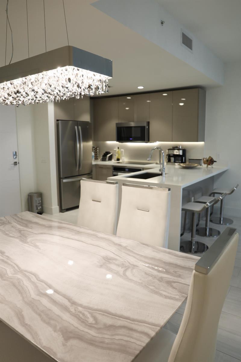 A modern kitchen features a stone-topped dining table, white chairs, and stainless steel appliances — 2000 Metropica Way # 811, Sunrise FL 33323, SUNRISE, FL