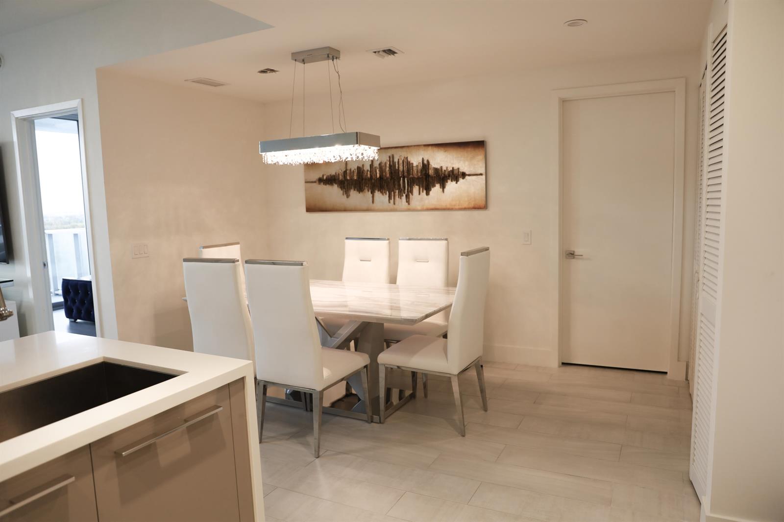 A dining area features a marble table, white chairs, a crystal chandelier, and abstract wall art — 2000 Metropica Way # 811, Sunrise FL 33323, SUNRISE, FL