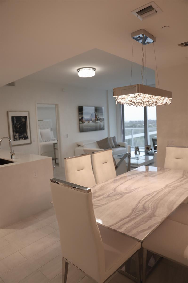 A dining area with a stone table and crystal chandelier overlooks a modern living room — 2000 Metropica Way # 811, Sunrise FL 33323, SUNRISE, FL