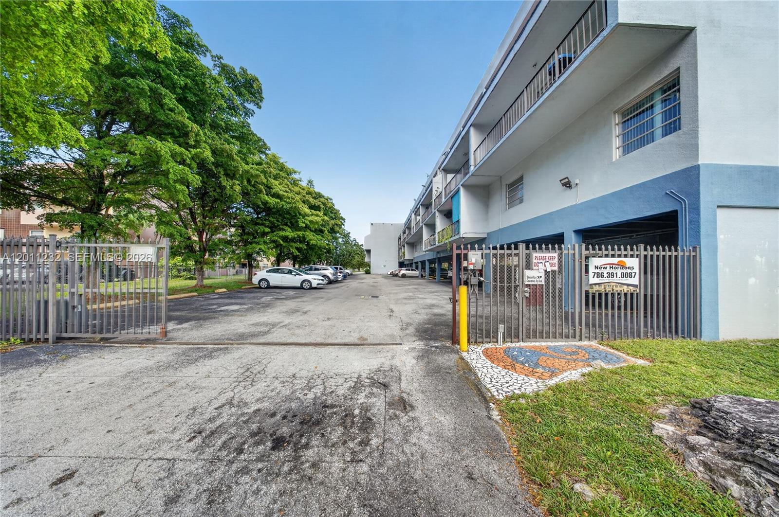A paved parking lot sits between a multi-story apartment building and a metal fence — 399 NW 72nd Ave # 209, Miami FL 33126, MIAMI, FL