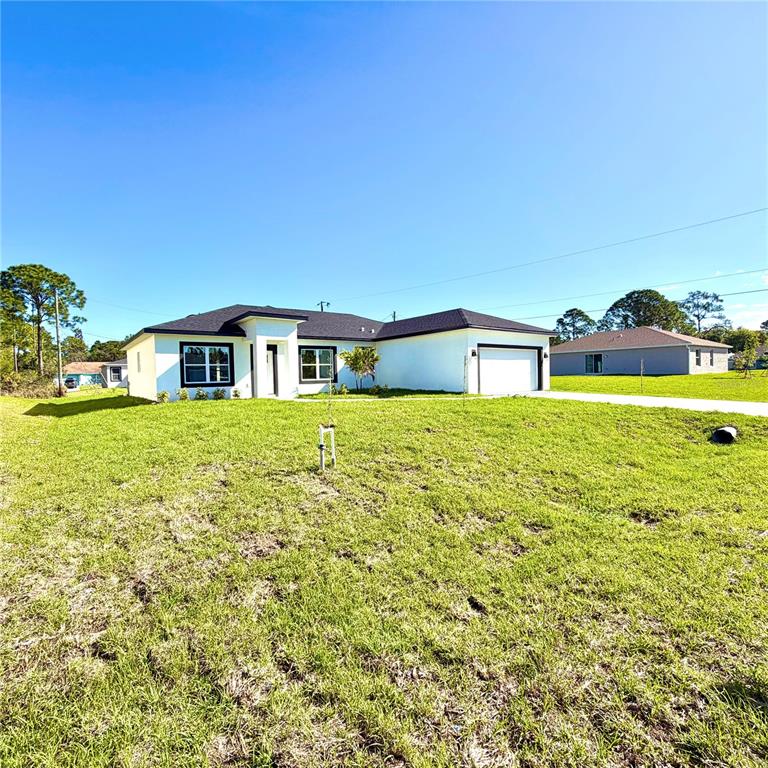 A white single-story house with a black roof and attached garage sits on a lawn — 487 ALAMO STREET SE, PALM BAY, FL