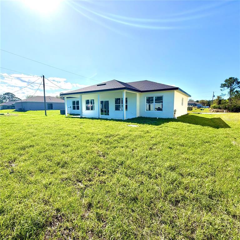 The exterior of a light-colored, single-story house features a covered patio and a grassy yard — 487 ALAMO STREET SE, PALM BAY, FL