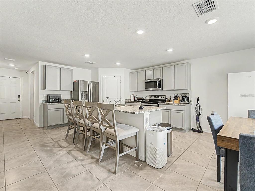 A kitchen features gray cabinets, granite countertops, a central island with seating, and tile flooring — 13484 MYLION WAY, SPRING HILL, FL