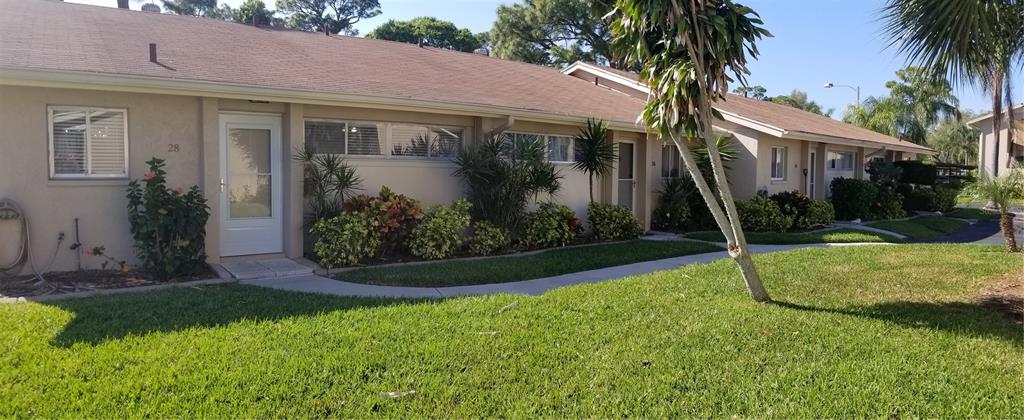 A row of single-story tan residential units with brown roofs and landscaped front yards — 2772 WOODGATE LANE UNIT 28, SARASOTA, FL