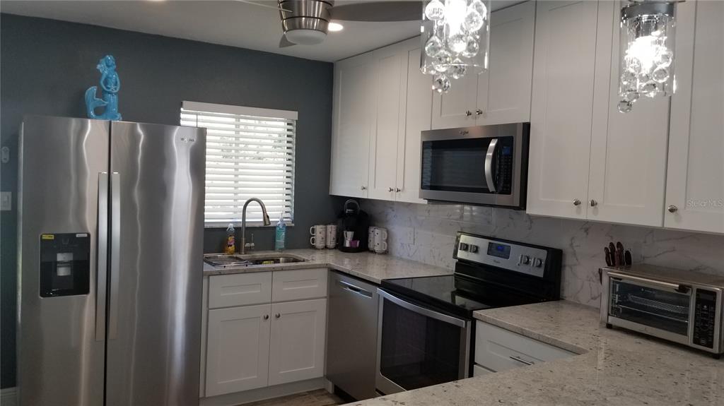 A kitchen features white cabinets, stainless steel appliances, and light-colored speckled countertops — 2772 WOODGATE LANE UNIT 28, SARASOTA, FL