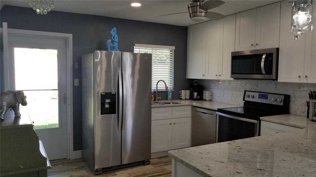 A kitchen features white cabinets, stainless steel appliances, granite countertops, and a dark accent wall — 2772 WOODGATE LANE UNIT 28, SARASOTA, FL