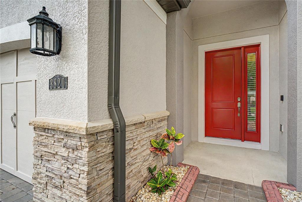 A red front door is adjacent to a stone-accented wall with a downspout and address — 3820 BOWFIN TRAIL, KISSIMMEE, FL