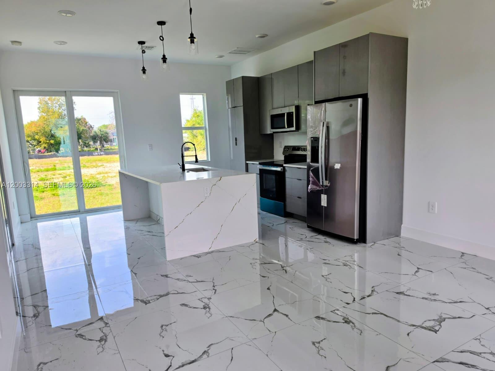A modern kitchen features gray cabinets, a marble-patterned island, and white marble-look tile flooring — 402 Harrison Dr, Lehigh Acres FL 33936, LEHIGH ACRES, FL