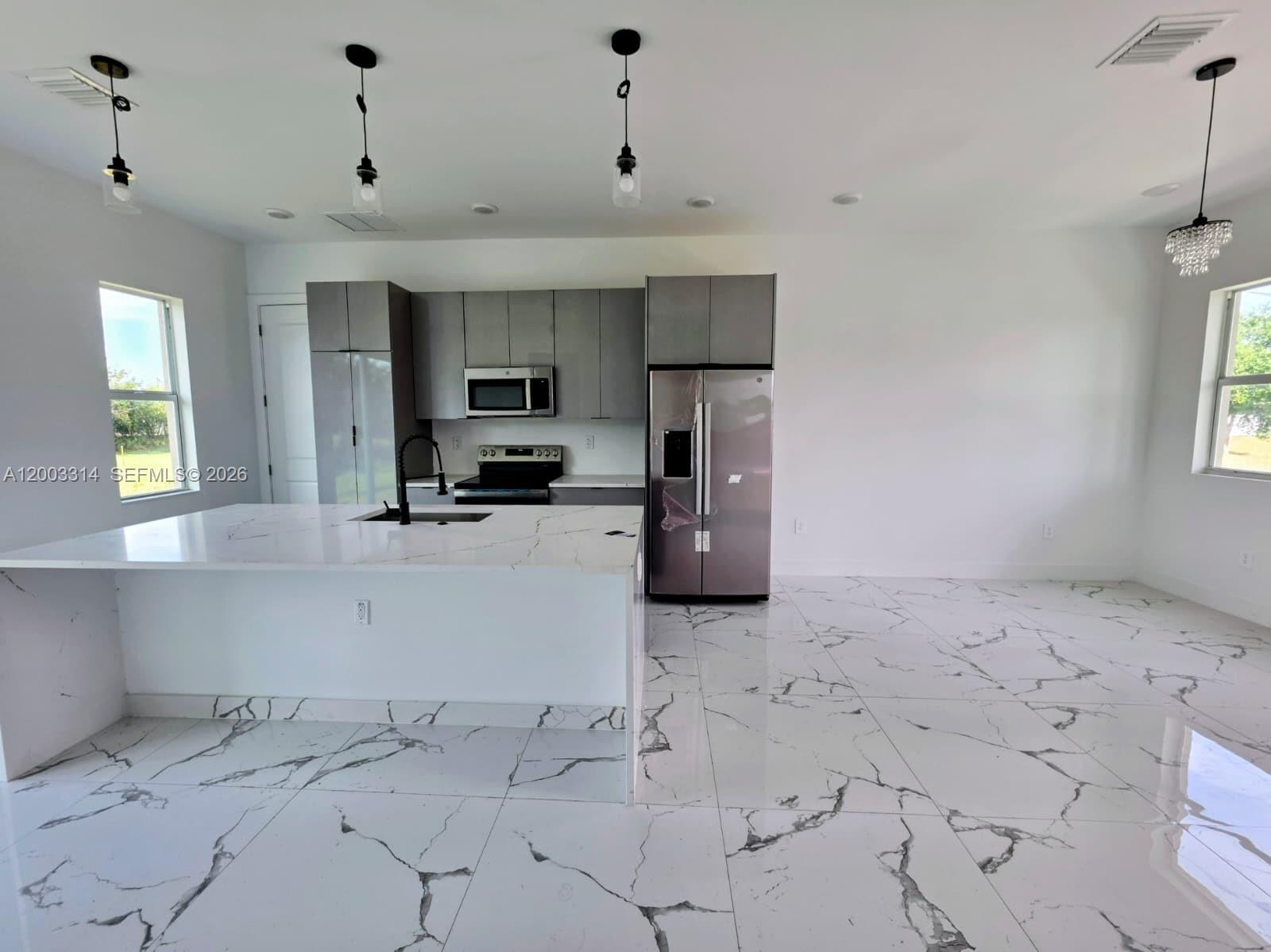 A modern kitchen features gray cabinetry, a white marble-patterned island, and matching tiled flooring — 402 Harrison Dr, Lehigh Acres FL 33936, LEHIGH ACRES, FL