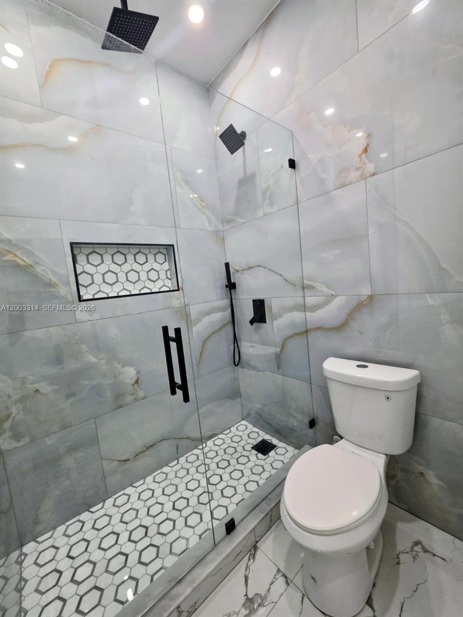 A bathroom features a glass-enclosed shower with marble-look tile, a hexagonal floor, and a toilet — 402 Harrison Dr, Lehigh Acres FL 33936, LEHIGH ACRES, FL