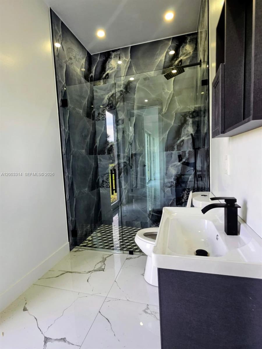 A bathroom features a glass-enclosed shower with dark marble-patterned tiles and a white vanity — 402 Harrison Dr, Lehigh Acres FL 33936, LEHIGH ACRES, FL