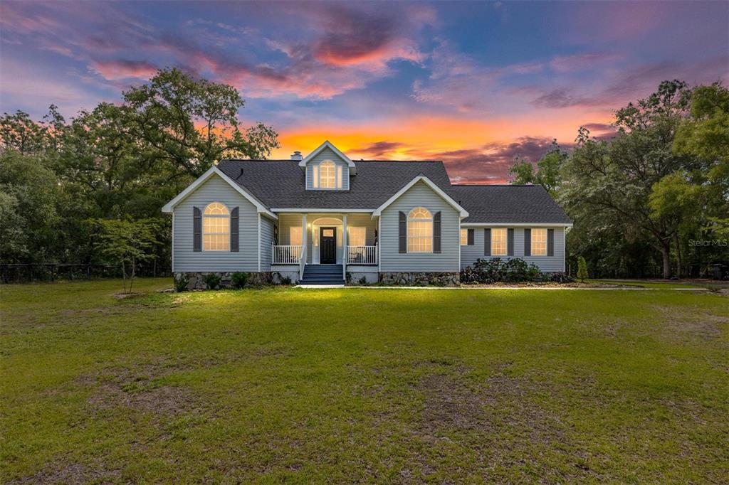A light gray house with a stone foundation and a front porch at sunset — 5801 SW 140TH AVENUE, OCALA, FL