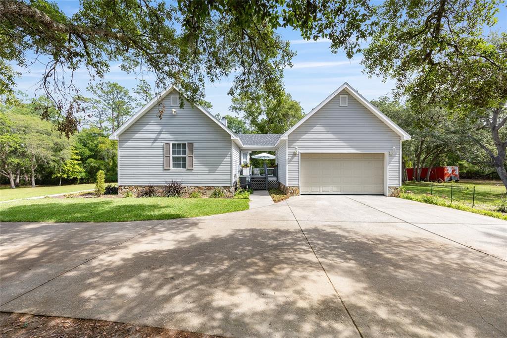 A light gray house with a two-car garage and a concrete driveway under large trees — 5801 SW 140TH AVENUE, OCALA, FL