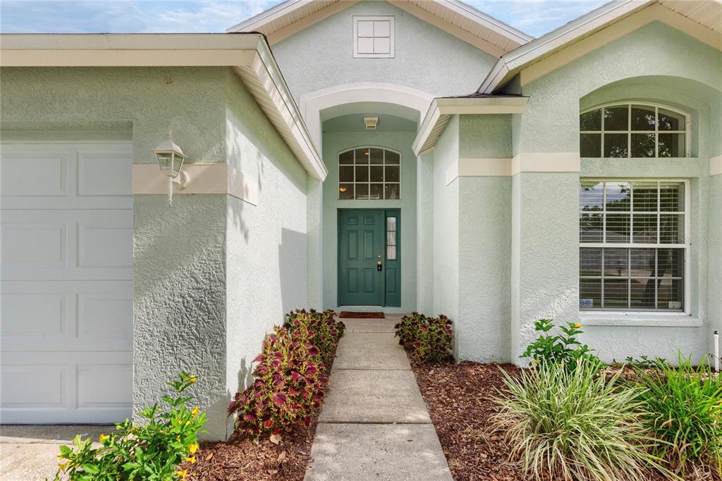 The exterior of a light green house features a teal front door and a walkway — 30446 TREMONT DRIVE, WESLEY CHAPEL, FL