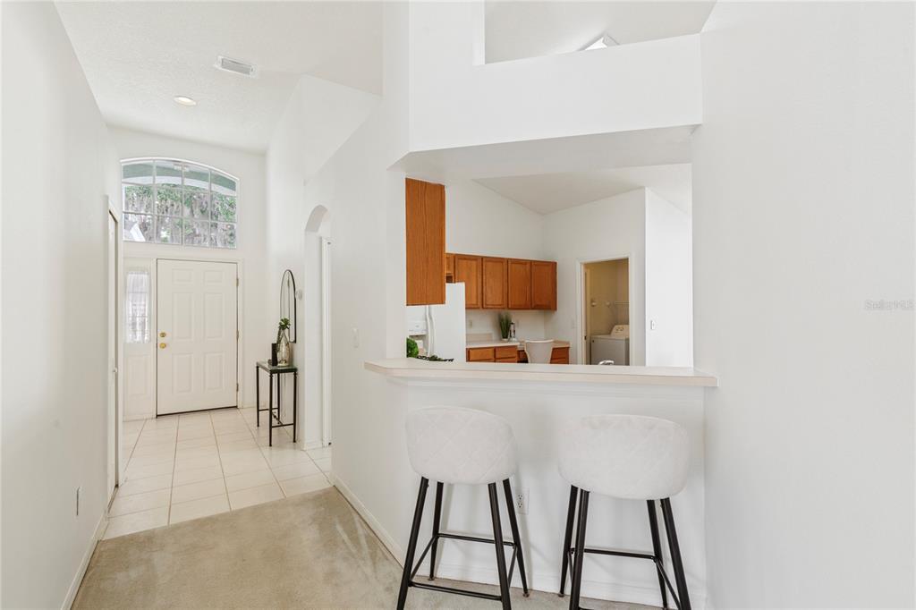 A view from a carpeted area toward a kitchen with a breakfast bar and stools — 30446 TREMONT DRIVE, WESLEY CHAPEL, FL