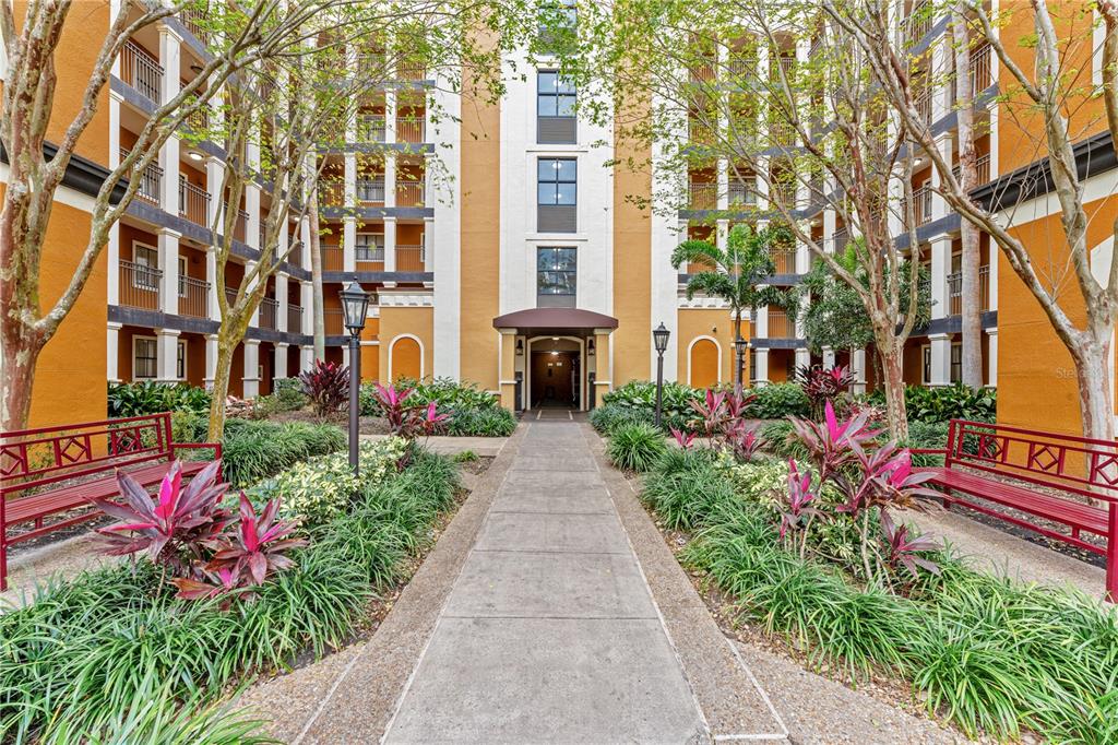 A concrete walkway leads to the entrance of a multi-story apartment building with red benches — 12544 FLORIDAYS RESORT DRIVE, ORLANDO, FL