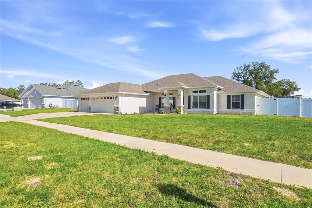 A single-story suburban house with a tan exterior, a three-car garage, and a large lawn — 12536 SUNSET WOODS DRIVE, SPRING HILL, FL