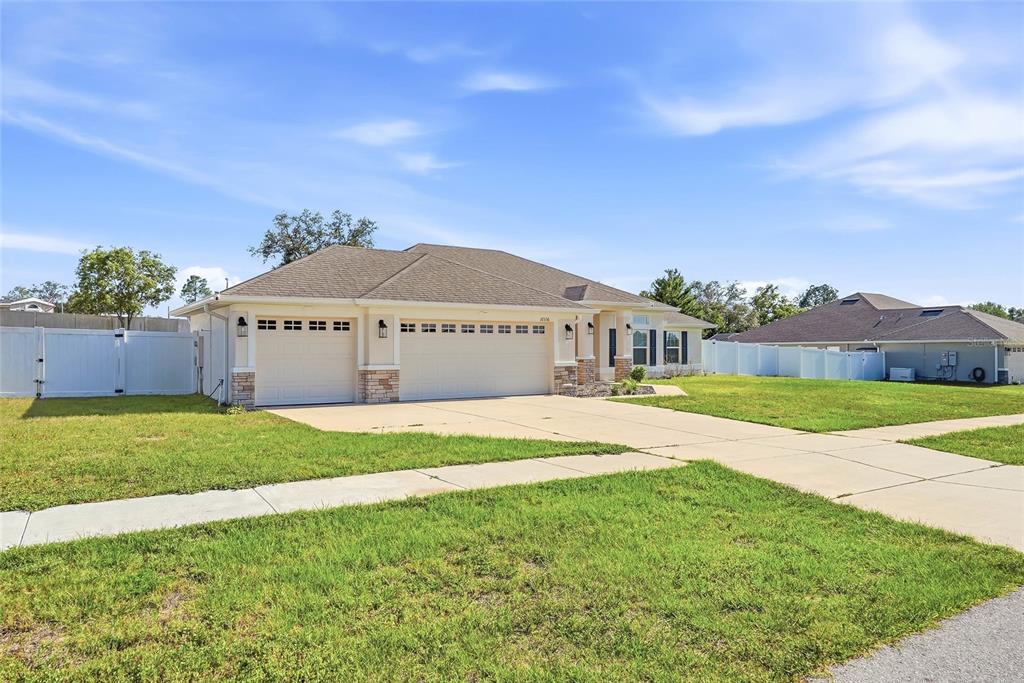 A single-story suburban house with a three-car garage and a white vinyl fence — 12536 SUNSET WOODS DRIVE, SPRING HILL, FL