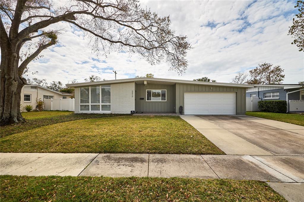 A single-story house with a white garage, gray siding, and a large tree in front — 3312 NAKORA DRIVE, TAMPA, FL