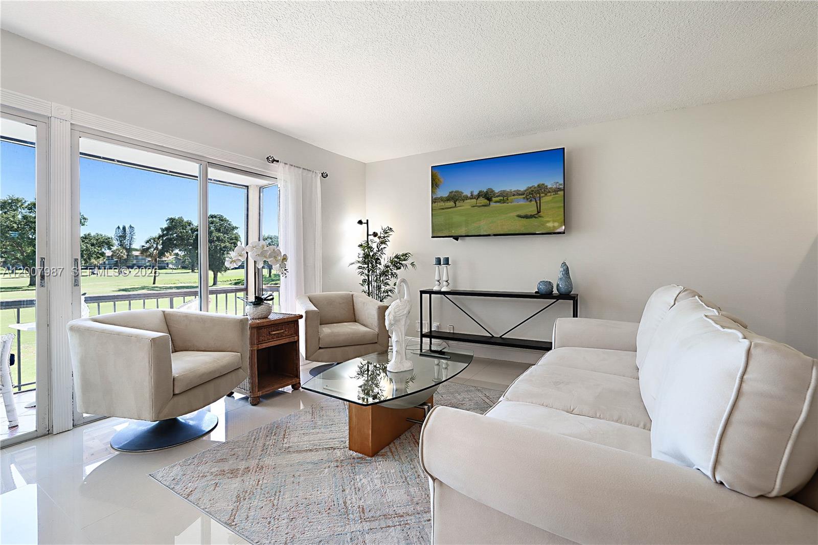 A living room features a white sofa, two armchairs, a glass coffee table, and golf course views — 9169 SE Riverfront Ter # M, Jupiter FL 33469, JUPITER, FL