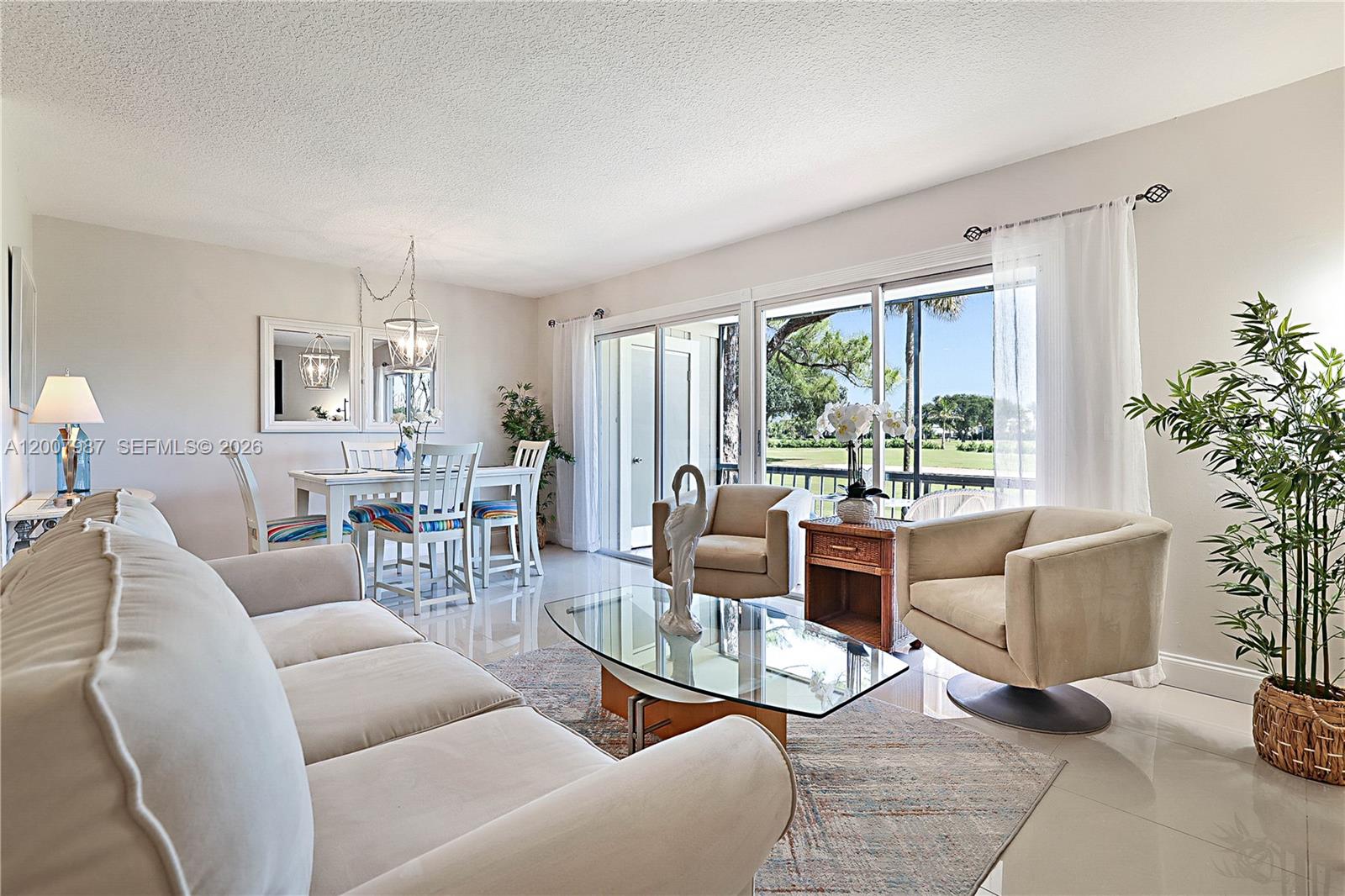 A living and dining room features light-colored furniture, a glass coffee table, and sliding doors — 9169 SE Riverfront Ter # M, Jupiter FL 33469, JUPITER, FL