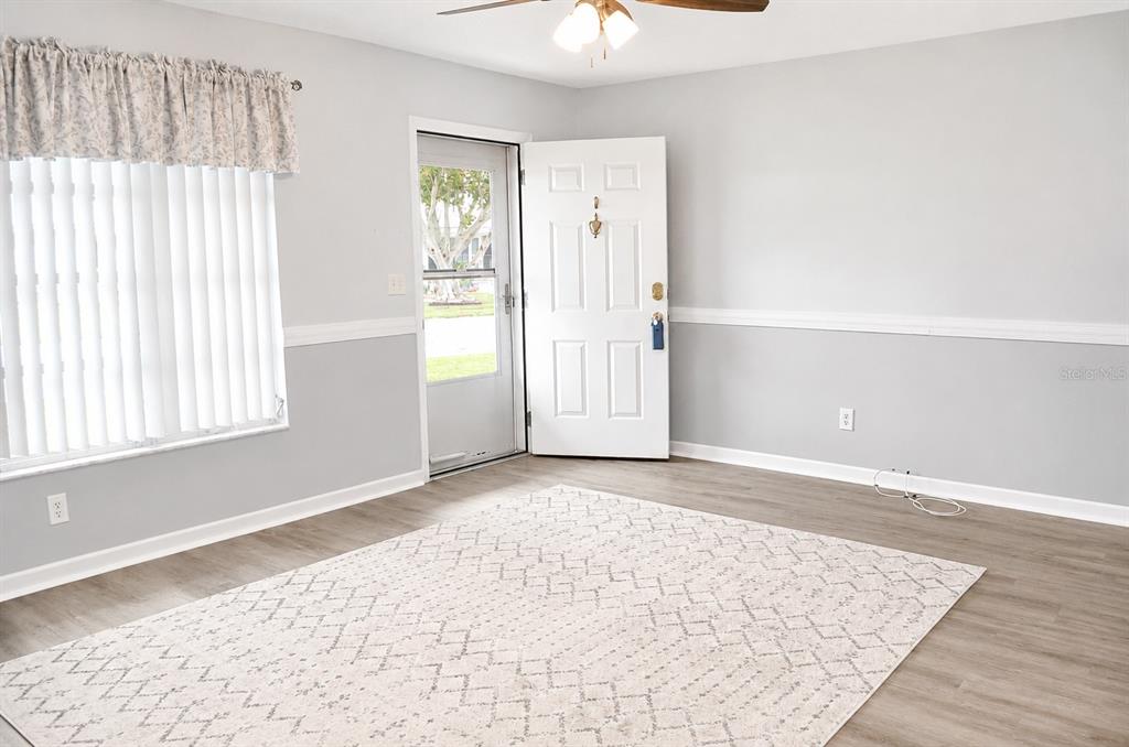 A living room features light gray walls, wood-look flooring, a large rug, and an entry door — 9632 42ND STREET N, PINELLAS PARK, FL