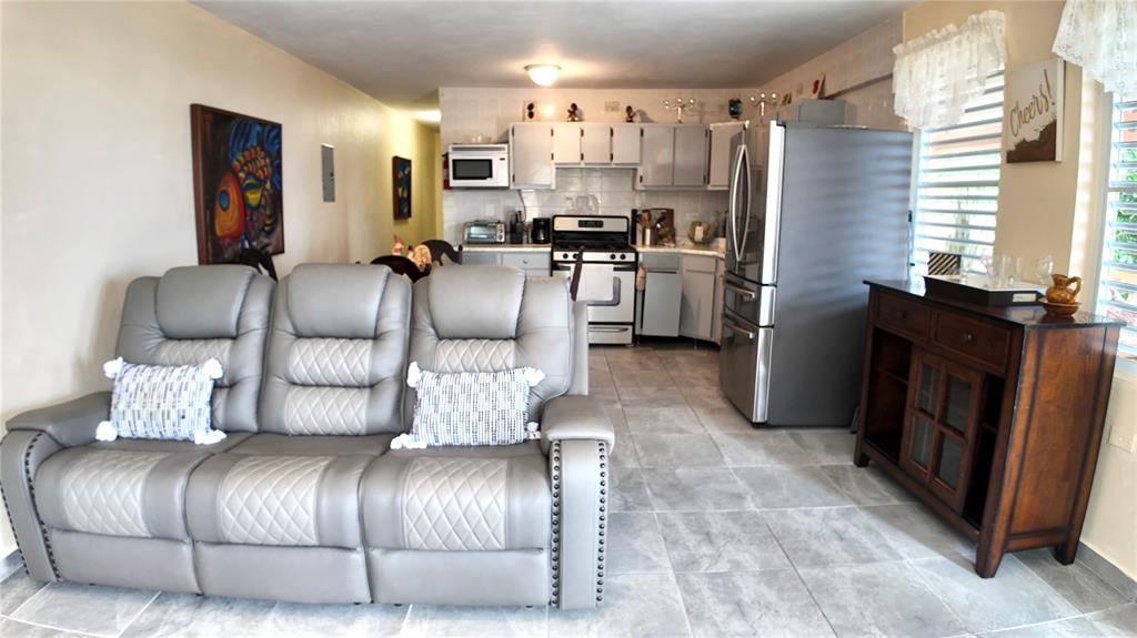 A living room with a gray reclining sofa opens into a kitchen with stainless appliances — Buzon 6312 Bo. Jaguay CARR. 412 KM 6.0, RINCON, PR