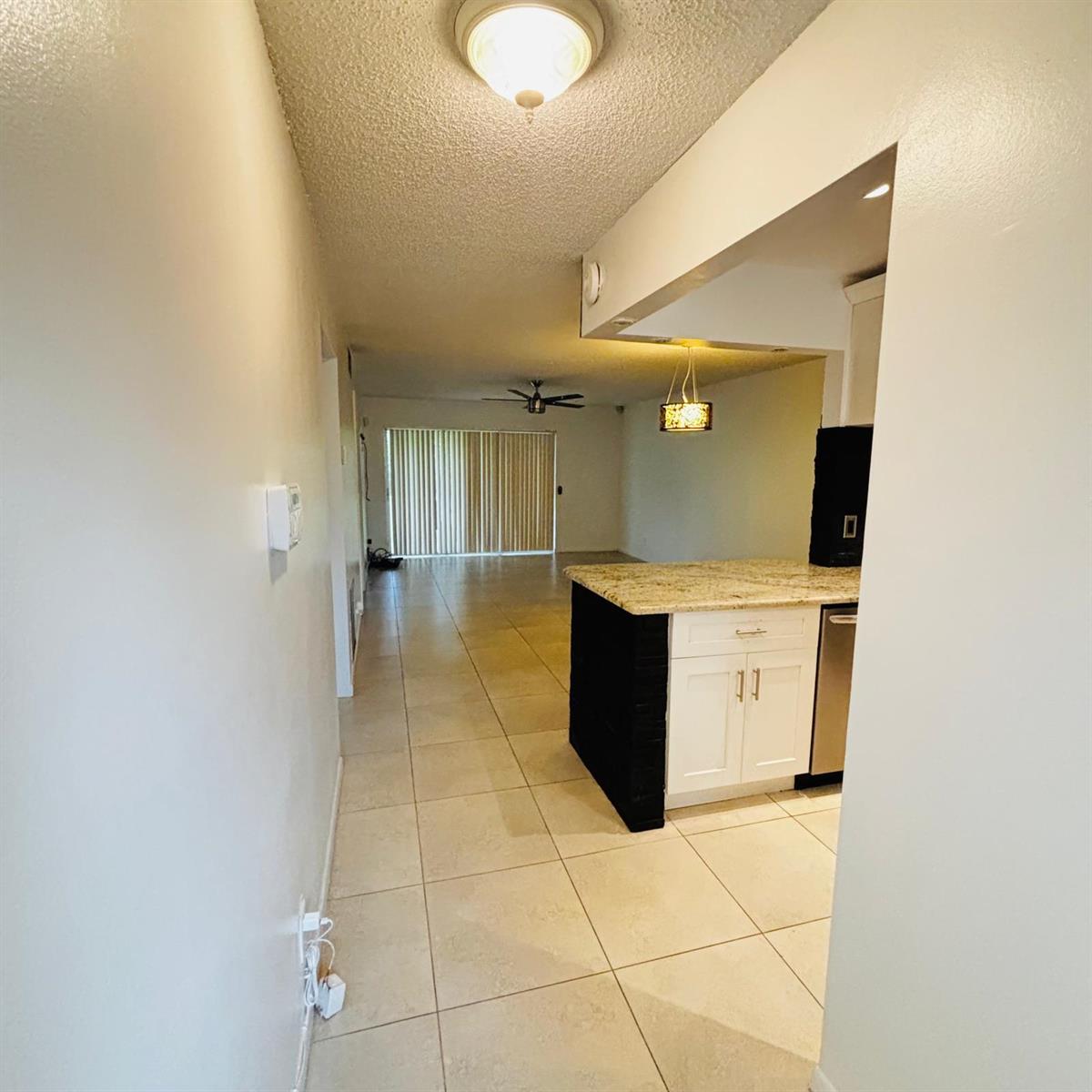 A view from a hallway into a kitchen with a granite-topped island and living area — 386 Bennington Lane, Lake Worth FL 33467, LAKE WORTH, FL