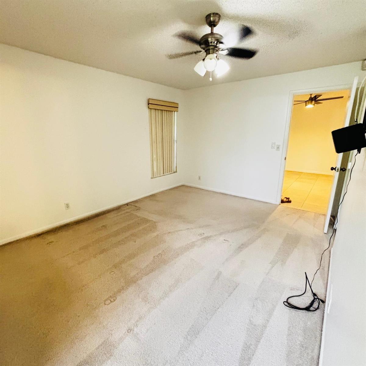 An empty bedroom features beige carpet, white walls, a ceiling fan, and a window — 386 Bennington Lane, Lake Worth FL 33467, LAKE WORTH, FL