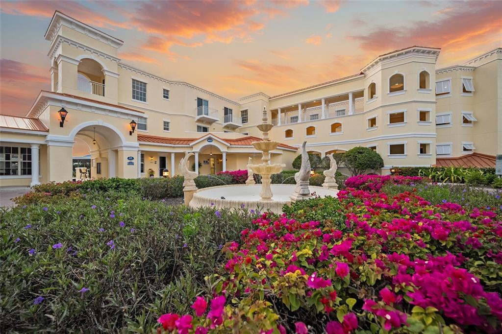 A multi-story Mediterranean-style building features a central fountain surrounded by vibrant pink bougainvillea flowers — 14021 BELLAGIO WAY UNIT 309, OSPREY, FL