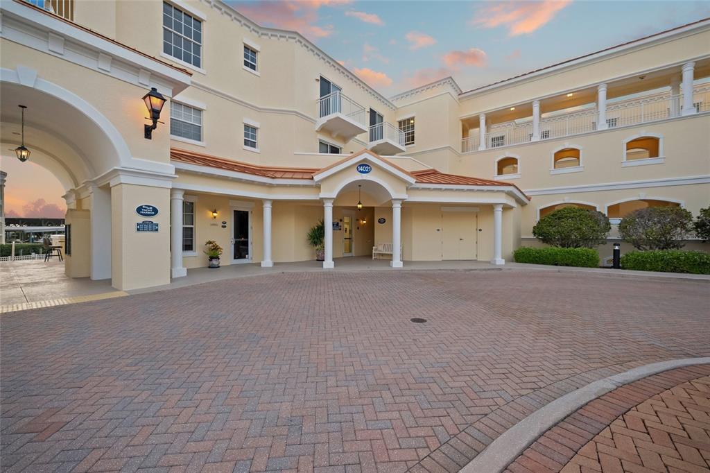 A paved circular driveway leads to the entrance of a multi-story yellow stucco building — 14021 BELLAGIO WAY UNIT 309, OSPREY, FL