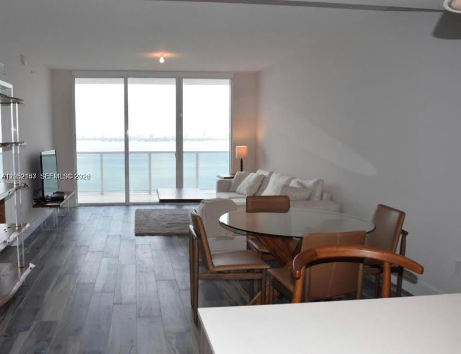 A modern living and dining area features wood-look tile floors and a balcony overlooking water — 600 NE 27th St # 2202, Miami FL 33137, MIAMI, FL