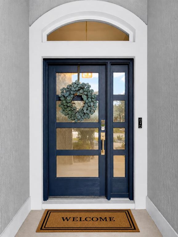 A dark blue front door with glass panels and a wreath sits under an arched transom — 2165 GORDON PATH, THE VILLAGES, FL