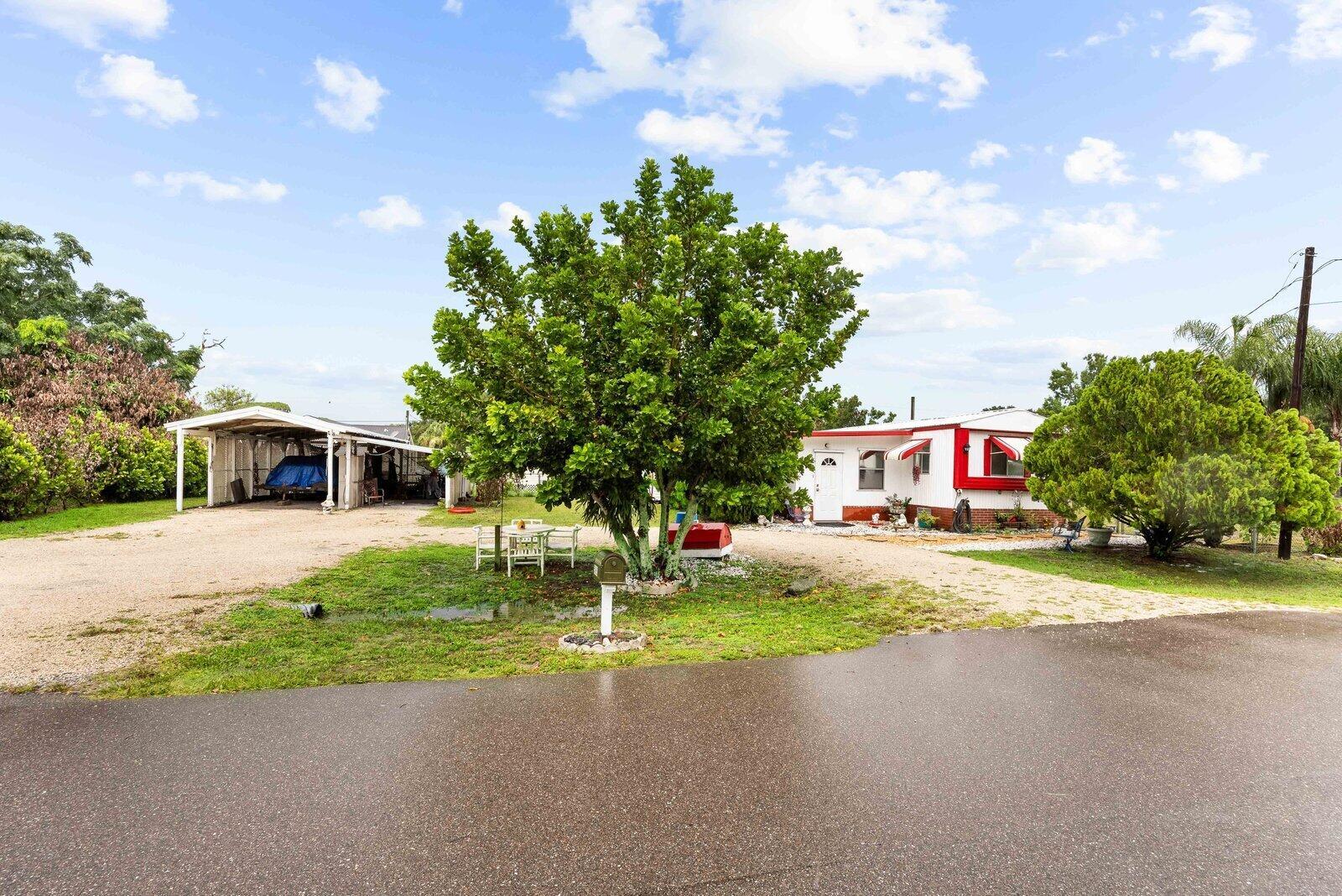 A single-story mobile home with a carport and a large tree in the front yard — 5985 SE 94TH Trail, Okeechobee FL 34974, OKEECHOBEE, FL