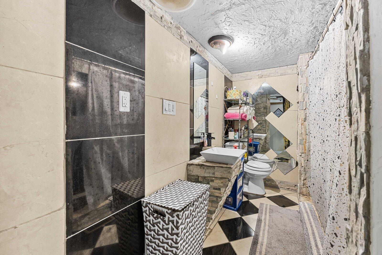 A bathroom features a vessel sink, stone-tiled vanity, black and white floor, and mirrored wall — 5985 SE 94TH Trail, Okeechobee FL 34974, OKEECHOBEE, FL