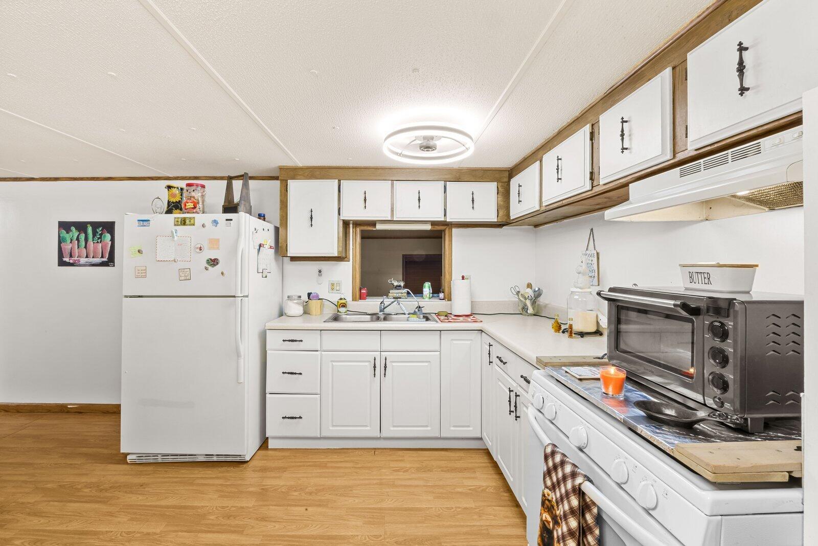 A kitchen features white cabinets, a white refrigerator, a toaster oven, and light wood flooring — 5985 SE 94TH Trail, Okeechobee FL 34974, OKEECHOBEE, FL