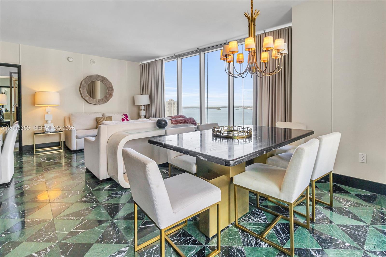 A dining area with a marble table and chairs sits before a living room with water views — 485 Brickell Ave # 2508, Miami FL 33131, MIAMI, FL