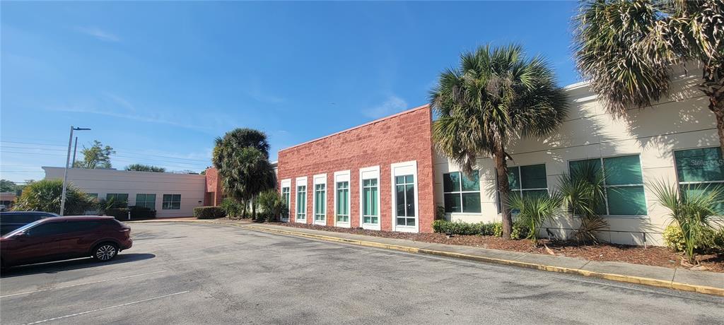 A low-rise commercial building features a red brick facade, white trim, and palm trees — 1277 SEMORAN BLVD UNIT 118, ORLANDO, FL