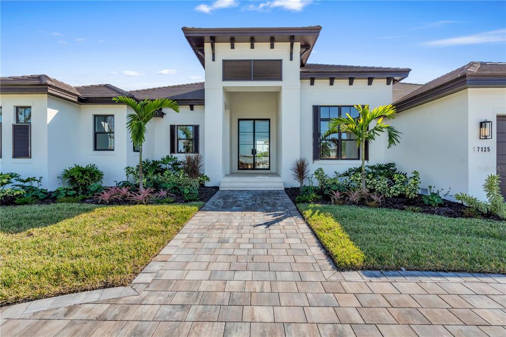 A modern single-story house features a paved walkway leading to a central glass-paneled front door — 7125 WESTMORELAND DRIVE, SARASOTA, FL